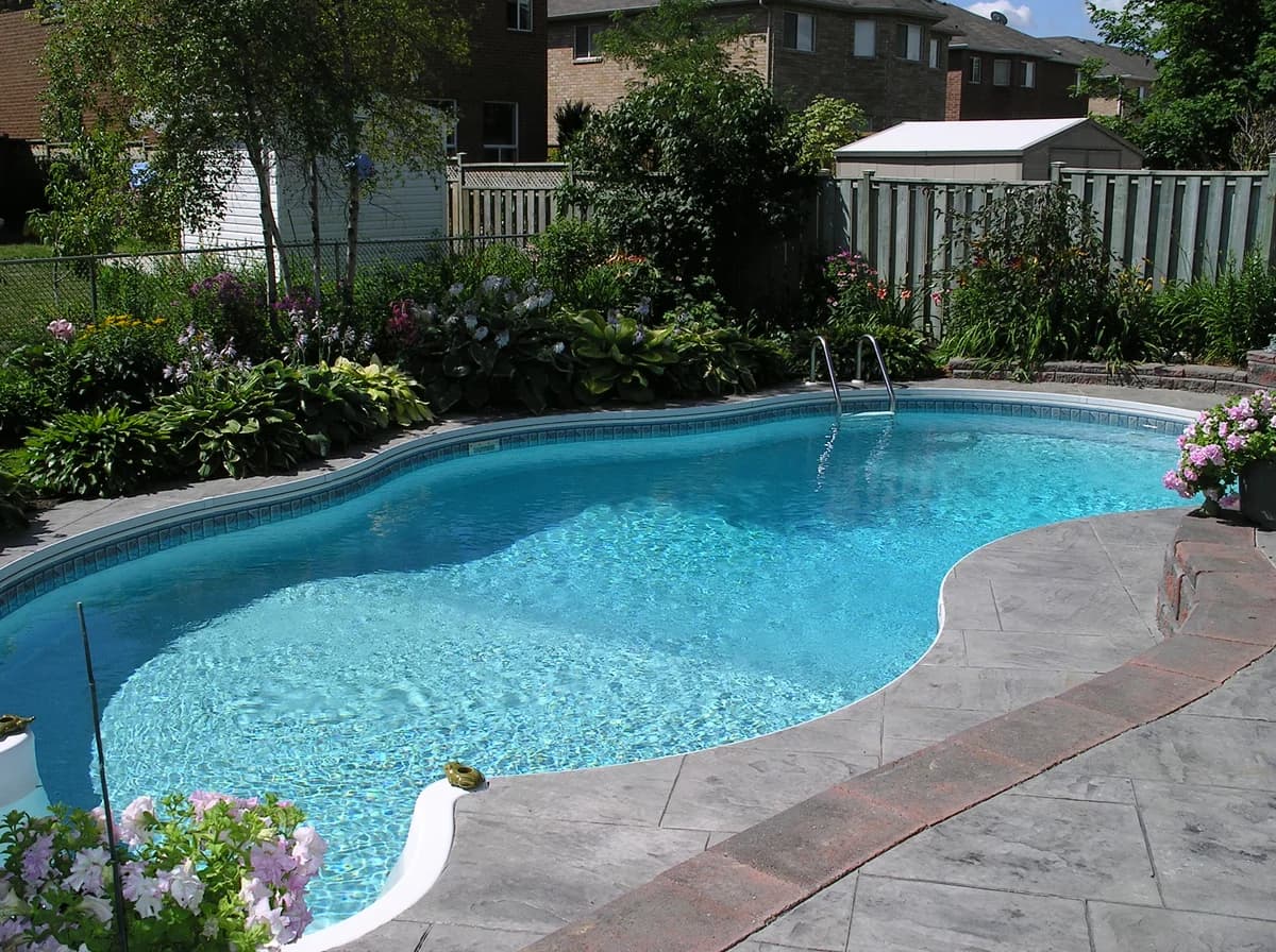 A pristine residential backyard swimming pool with crystal clear water and stamped concrete patio coping
