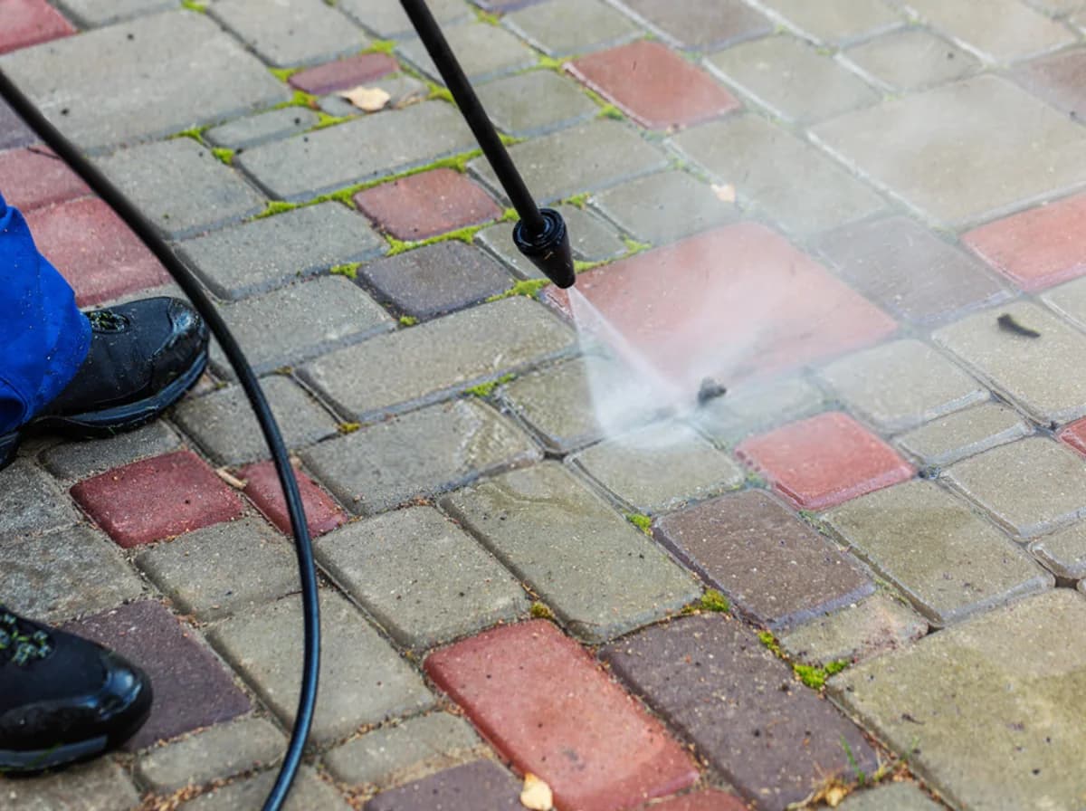 High-pressure washer wand cleaning pavers and driveway surfaces with water spray and moss removal